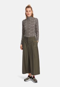 Leopard print turtleneck top, olive wide-leg trousers with large pockets, and black sneakers with a leopard pattern and pink accents.