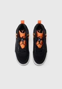 Scarpe da ginnastica nere con dettagli arancioni, tomaia in tessuto, suole in gomma e collare imbottito; presentano un'unità Air visibile e un sistema di lacci.