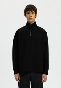 Pull-over noir à col zippé, fabriqué en tissu doux, avec des manches longues et une coupe décontractée, doté d'une fermeture éclair argentée et de poignets côtelés.