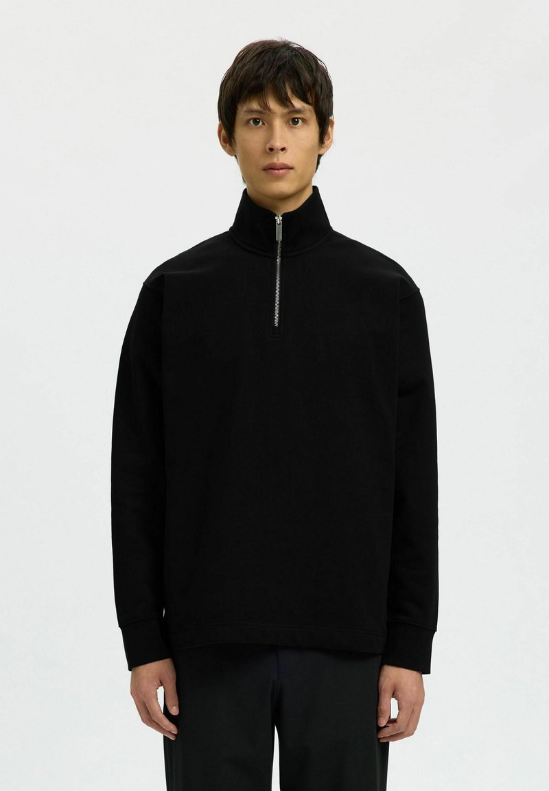 Pull-over noir à col zippé, fabriqué en tissu doux, avec des manches longues et une coupe décontractée, doté d'une fermeture éclair argentée et de poignets côtelés.