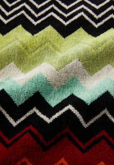 Tessuto colorato con motivo a zigzag nelle tonalità di verde, nero, rosso e bianco, caratterizzato da una superficie morbida e testurizzata.