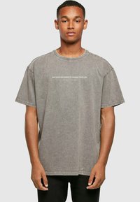 Grijze oversized T-shirt van katoen, met een ronde hals en korte mouwen, met de tekst "JE HEBT DE KRAFT OM JOUW LEVEN TE VERANDEREN" gedrukt over de borst.