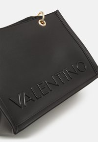 Schwarze Lederhandtasche mit geprägt Logo, goldenen Beschlägen und strukturiertem Design mit glatter Textur. Geeignet für verschiedene Anlässe.