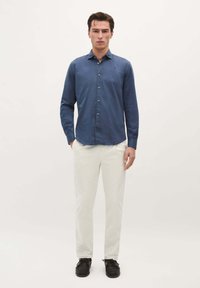 Blaues Hemd mit langen Ärmeln, weiße Hose und schwarze Schuhe, präsentiert vor einem neutralen Hintergrund.
