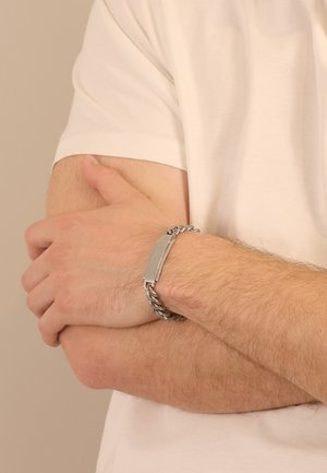 Silver chain bracelet with a flat rectangular metal plate. The bracelet features interlinked chain links and a smooth, polished texture.