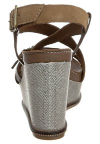 Sandale à talon compensé en suède marron avec une bride à la cheville, présentant un talon en motif herringbone argenté, une forme courbée et une semelle texturée robuste.