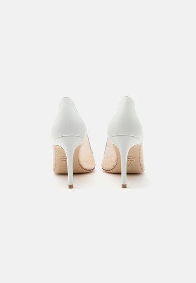 Chaussures blanches à talons hauts avec des talons fins et un détail en dentelle sur les côtés, vues de dos sur une surface blanche unie.