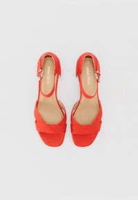 Rote Wildleder-Sandalen mit einem Kreuzriemendesign, offener Ferse und silberner Schnalle. Flache Sohle und gepolstertes Fußbett.