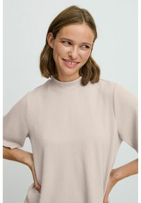 Lys beige ribbet striktop med høj hals og korte ærmer, der har en afslappet pasform og blød tekstur.