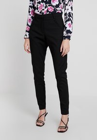 Pantalon noir ajusté au design épuré, en tissu lisse, avec des poches avant taillées, associé à un haut à manches longues à motif floral.