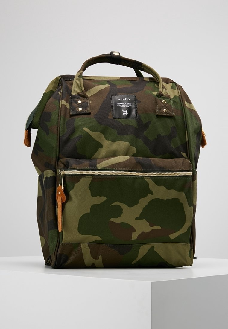 Kamuflaasi-kuvioinen reppu, jossa on ylhäällä kantokahvat, edessä vetoketjullinen tasku ja musta etiketti, jossa lukee "anello", valkoisella pinnalla.