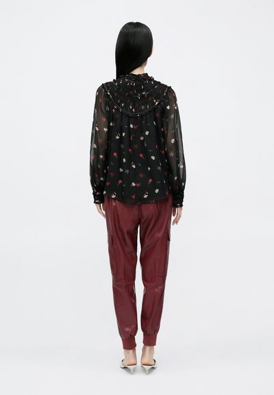 Camicia nera trasparente con stampa floreale e colletto arricciato abbinata a pantaloni cargo color bordeaux in ecopelle con polsini elastici e tasche laterali.