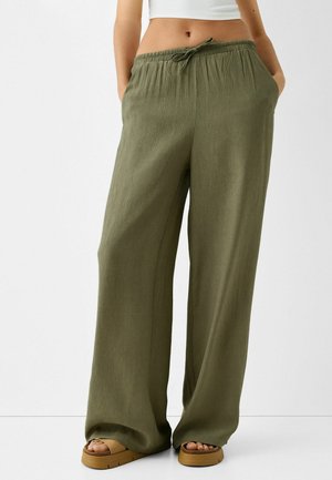 Luchtige broek in olijfgroen met gestructureerde stof en trekkoord in de taille, gecombineerd met beige platformsandalen en een wit cropped topje.