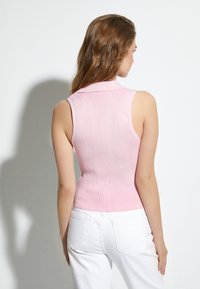 Top ajustado sin mangas de punto acanalado en rosa claro, con cuello tipo camiseta. Combinado con pantalones de mezclilla blancos.