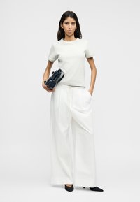 Ανοιχτό γκρι μπλούζα με υφή, λευκό παντελόνι με φαρδιά μπατζάκια και μαύρες μυτερές γόβες. Το μοντέλο κρατάει μια μικρή σκουρομπλε τσάντα.