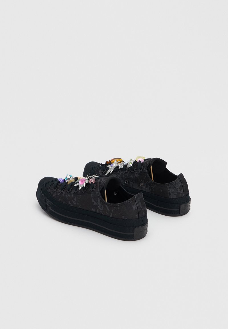 Pair of black low-top sneakers with floral patterns and colorful decorative charms on the laces, shown from the back and side on a white background.