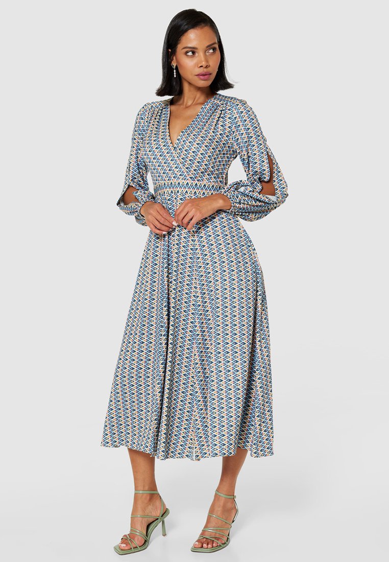Niebieska sukienka w kremowe wzory, zapinana na wstążki, z długimi rękawami, wycięciami w okolicy łokci i zwiewnym, średniej długości dołem.