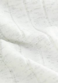 Vitt tyg med en mjuk, texturerad yta, prytt med fina, grå prickar och ett subtilt randigt mönster.