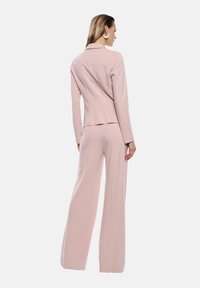 Set di completo rosa chiaro composto da una giacca aderente con maniche lunghe e pantaloni a gamba larga, realizzati in un tessuto liscio con una finitura elegante.