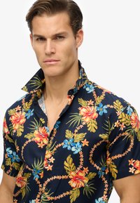 Camicia a maniche corte floreale in blu navy con vivaci fiori rossi, gialli e blu. Materiale in cotone con colletto e dettagli con bottoni.