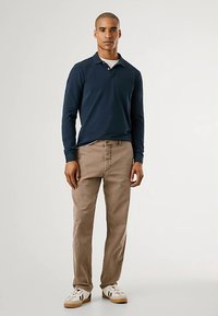 Polo de manga comprida azul-marinho com gola, combinado com chinos castanho-claro e ténis brancos. Tecido suave com design ajustado.