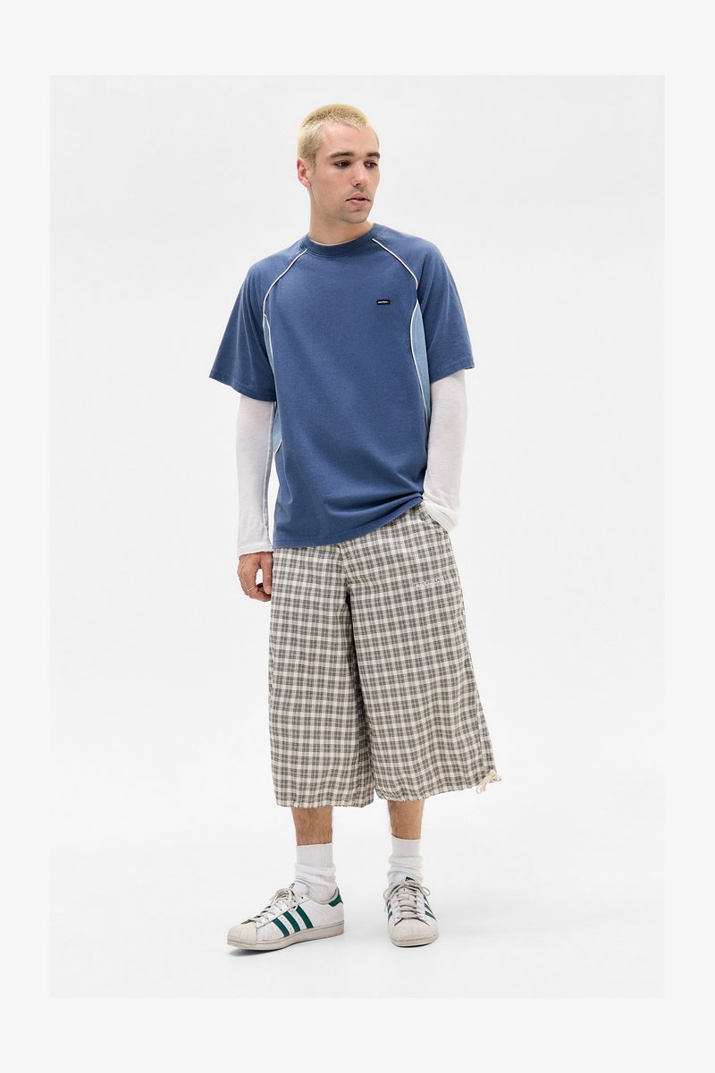 Blå T-shirt med lyseblå detaljer, rutede shorts og hvide sneakers med grønne accenter. Korte ærmer og afslappet pasform.