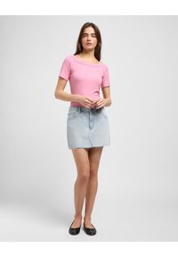 T-shirt rose clair à rayures avec des manches courtes, associé à une mini-jupe en denim clair avec un ourlet effiloché, et des chaussures plates noires.