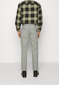 Plaid shirt in green and black, paired with gray trousers. Trousers feature back pockets and a branded tag. Black shoes complete the look.