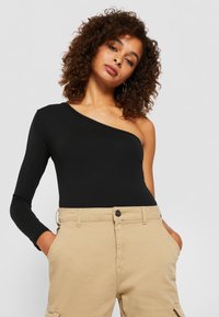 Mustat olkahihnatont bodysuit pitkällä hihalla, sileä kangas, istuva muotoilu. Yhdistetty ruskehtaviin, korkeavyötäröisiin housuihin, joissa on etutaskut.