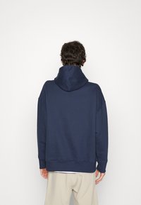 Felpa blu navy con cappuccio regolabile, vestibilità ampia, polsini e orlo a coste, e design minimalista. Tessuto morbido, stile casual.
