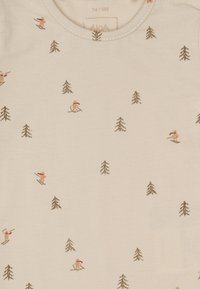 Helle beige Stoff mit weicher Textur, versehen mit einem Muster aus Skifahrern und Kiefern in Braun- und gedeckten Farben. Rundhalskragen.