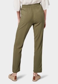 Pantaloni leggeri verde oliva, con vita elastica, gambe affusolate e tessuto liscio; abbinati a scarpe slip-on color cammello.