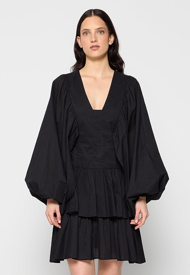 Schwarzes Kleid mit tiefem V-Ausschnitt, puffierten langen Ärmeln und gestuftem Rüschensaum. Hergestellt aus einem leichten Stoff mit glatter Textur.