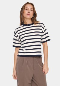T-shirt en tricot à rayures bleu marine et blanches à manches courtes avec un col ras du cou côtelé, associé à un pantalon marron taille haute. Texture douce.