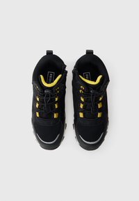 Melni un dzelteni sporta apavi ar sieti un auduma augšdaļu, elastīgām šņorēm un atstarojošiem elementiem, skatīti no augšas uz balta fona.