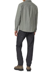 Overhemd met knopen van een zachte, groene, gestructureerde stof; gecombineerd met donkere denim jeans en bruine suède laarzen. Details van de rugpas zichtbaar.