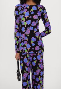 Zestaw z długim rękawem i spodniami z elastycznego materiału, z czarnym tłem i dużym niebiesko-różowym kwiatowym wzorem oraz zielonymi liśćmi.