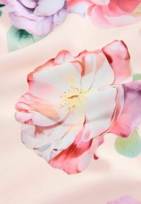 Miękka różowa tkanina z dużymi, szczegółowymi kwiatowymi wzorami w odcieniach bieli, różu, purpury oraz zielonych liści, ukazująca teksturę tkaniny i fałdy.