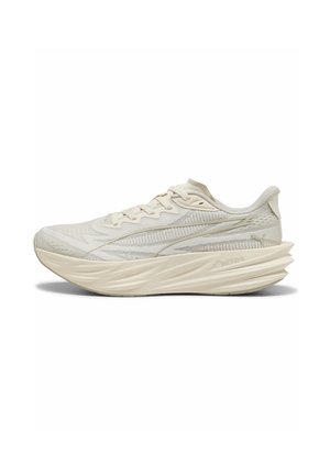 Zapatilla de running beige claro con parte superior de punto texturizado, suela gruesa y acolchada, diseño con cordones y una sutil franja de la marca en el lateral.