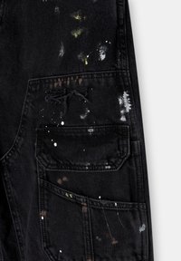 Pantalones cargo de mezclilla negra con salpicaduras de pintura en blanco, verde y marrón. Incluyen un bolsillo delantero con bordes desgastados y tela texturizada.