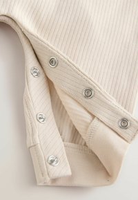 Tissu beige côtelé avec des boutons-pression en argent. Le matériau semble doux, avec une texture lisse et des bords finis.