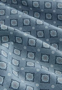 Hellblaues Gewebe mit einem wiederholten geometrischen Muster aus Quadraten, die mit floralen Motiven in Dunkelblau sowie Akzenten in Rosa und Weiß verziert sind.