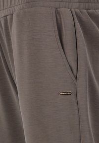 Pantalons de jogging légers gris avec poches latérales et taille élastique, arborant un petit logo métallique à l'avant. Texture lisse.