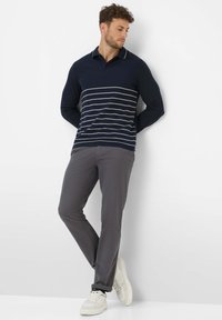 Marineblaue Langarm-Polohemd mit weißen horizontalen Streifen; kombiniert mit grauen Hosen und weißen Sneakers. Einfaches Design, klassische Farbgebung.