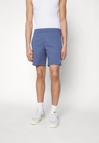 Blå träningsoveraller med resårmidja, sidofickor och en liten logodetalj. Matchas med vita sneakers och strumpor.