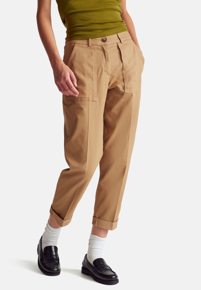 Beige kalhoty z bavlněné směsi s volným střihem, které mají dvě boční kapsy, jednu zadní kapsu a ohrnuté nohavice. V kombinaci s černými mokasíny a bílými ponožkami.