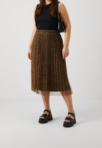 Brun plisserad midikjol med ett leopardmönster, parat med en svart linne och kraftiga svarta sandaler. Svart handväska hängande över axeln.