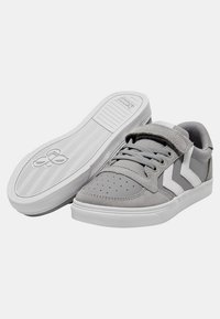 Sneaker in suede grigio e materiale sintetico con dettagli bianchi, dotati di punta perforata, chiusura con lacci e velcro, e suola in gomma.