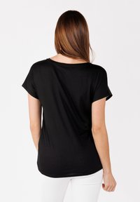 Camiseta negra de manga corta con un corte relajado, escote redondeado y textura suave, vista desde la parte posterior sobre un fondo sencillo.