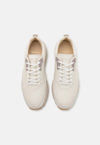 Hvite lær sneakers med perforerte detaljer, kontrasterende lysebrune accenter, gummisåler og flate hvite snørebånd.
